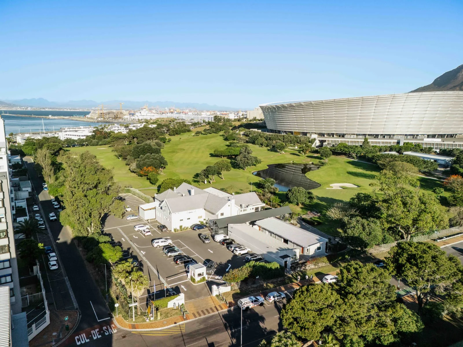 A white gabled building and car park beside the course and the stadium