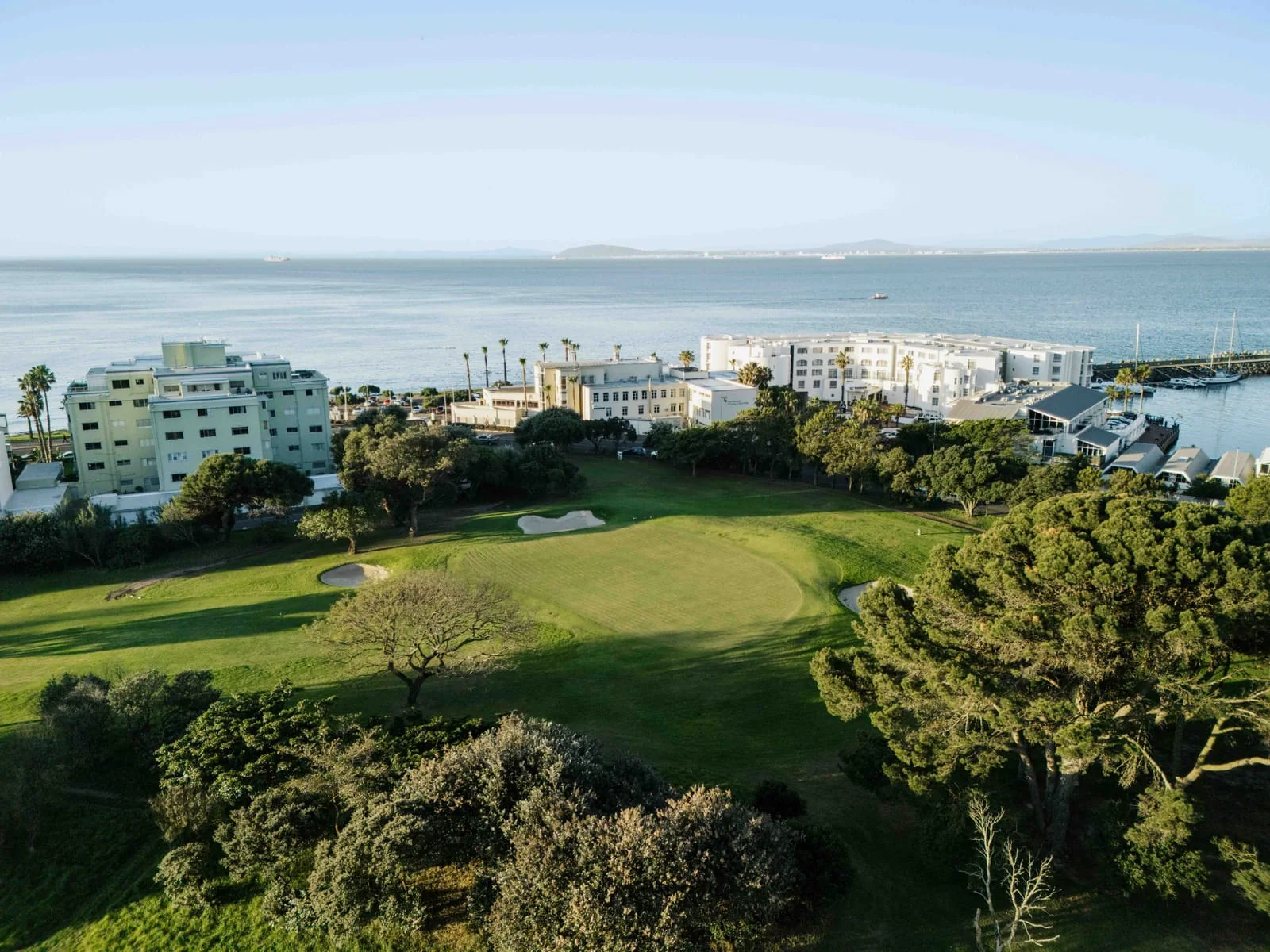 A green and its bunkers above the seafront, with the marina to the right
